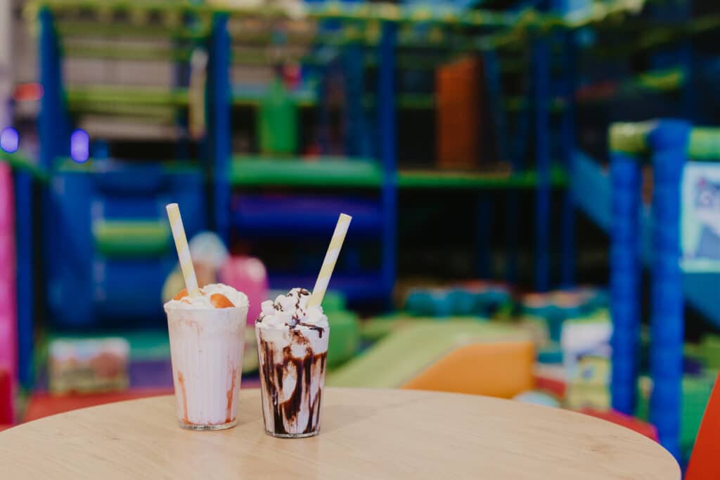 Two milkshakes on a café table with soft play in the background